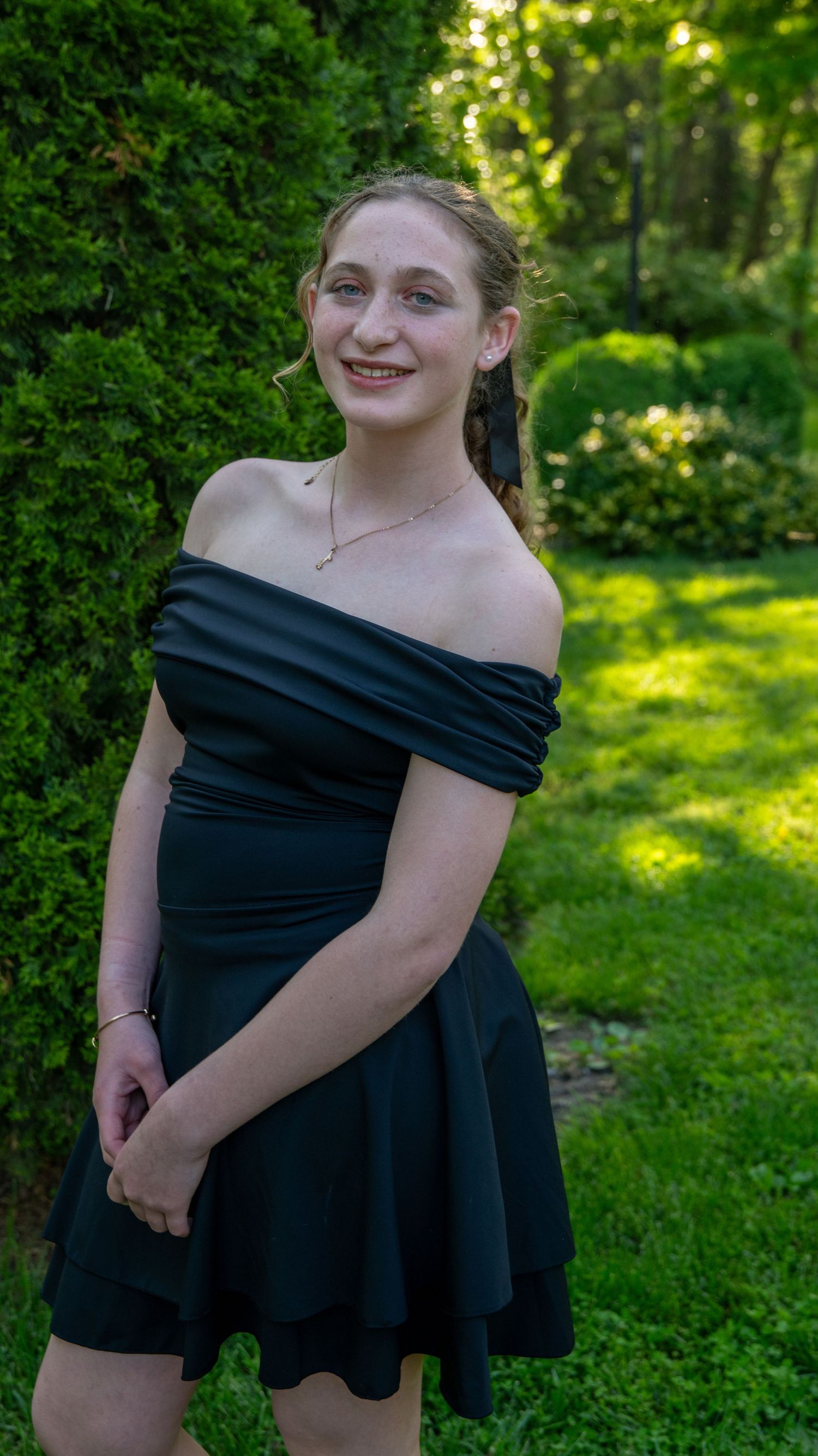A series of playful poses in a black off-shoulder dress against a lush green garden background.