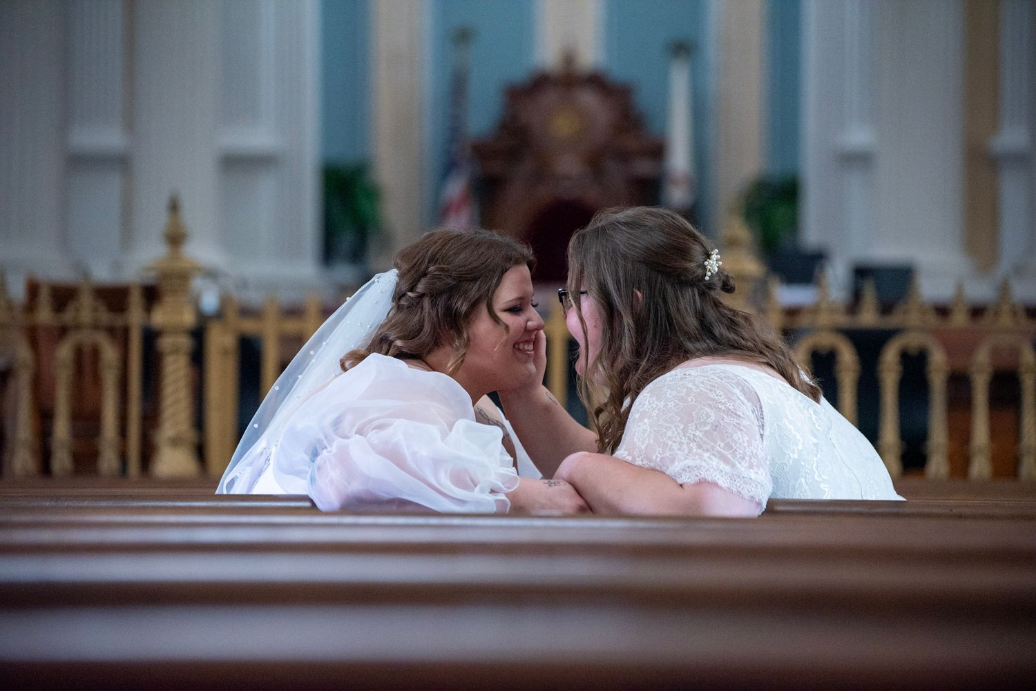 An intimate moment between two brides sharing a quiet conversation in a church pew.