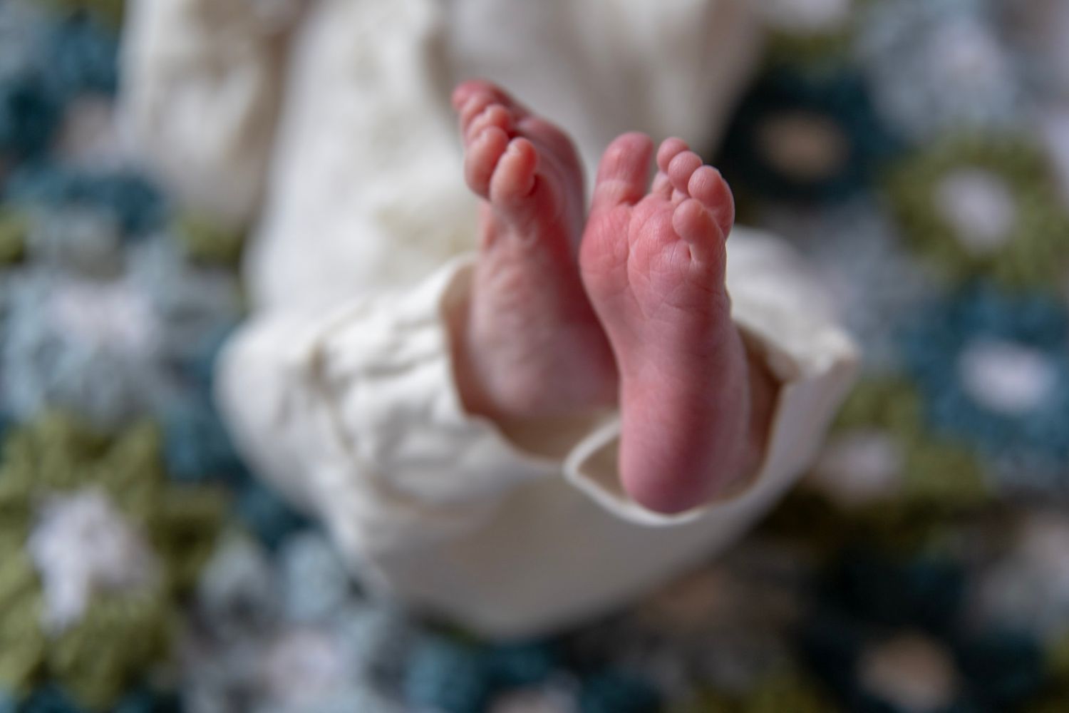Tiny baby feet wrapped in white fabric against soft background.