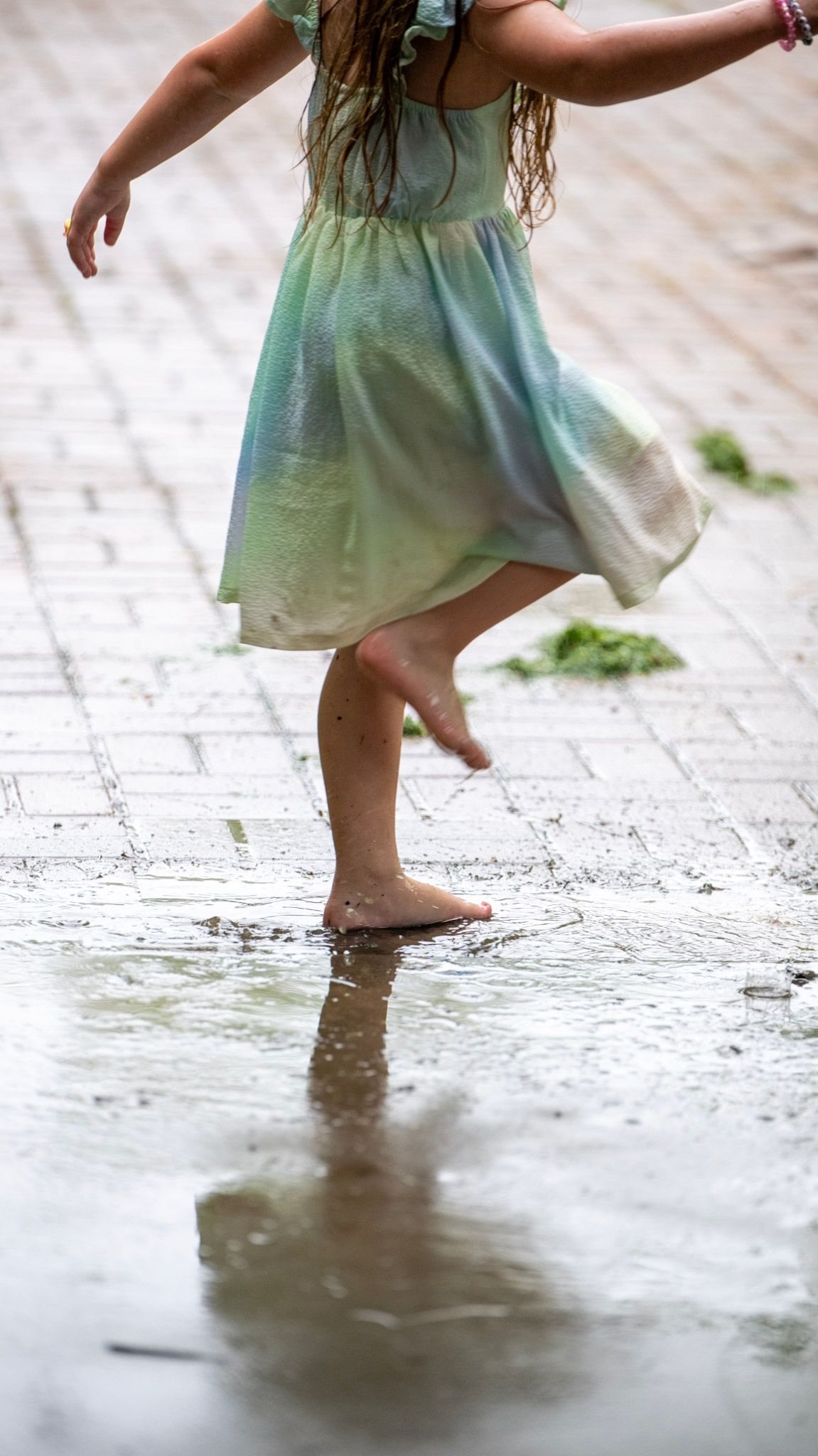 Close-up of bare feet splashing in puddles while wearing a mint green dress.