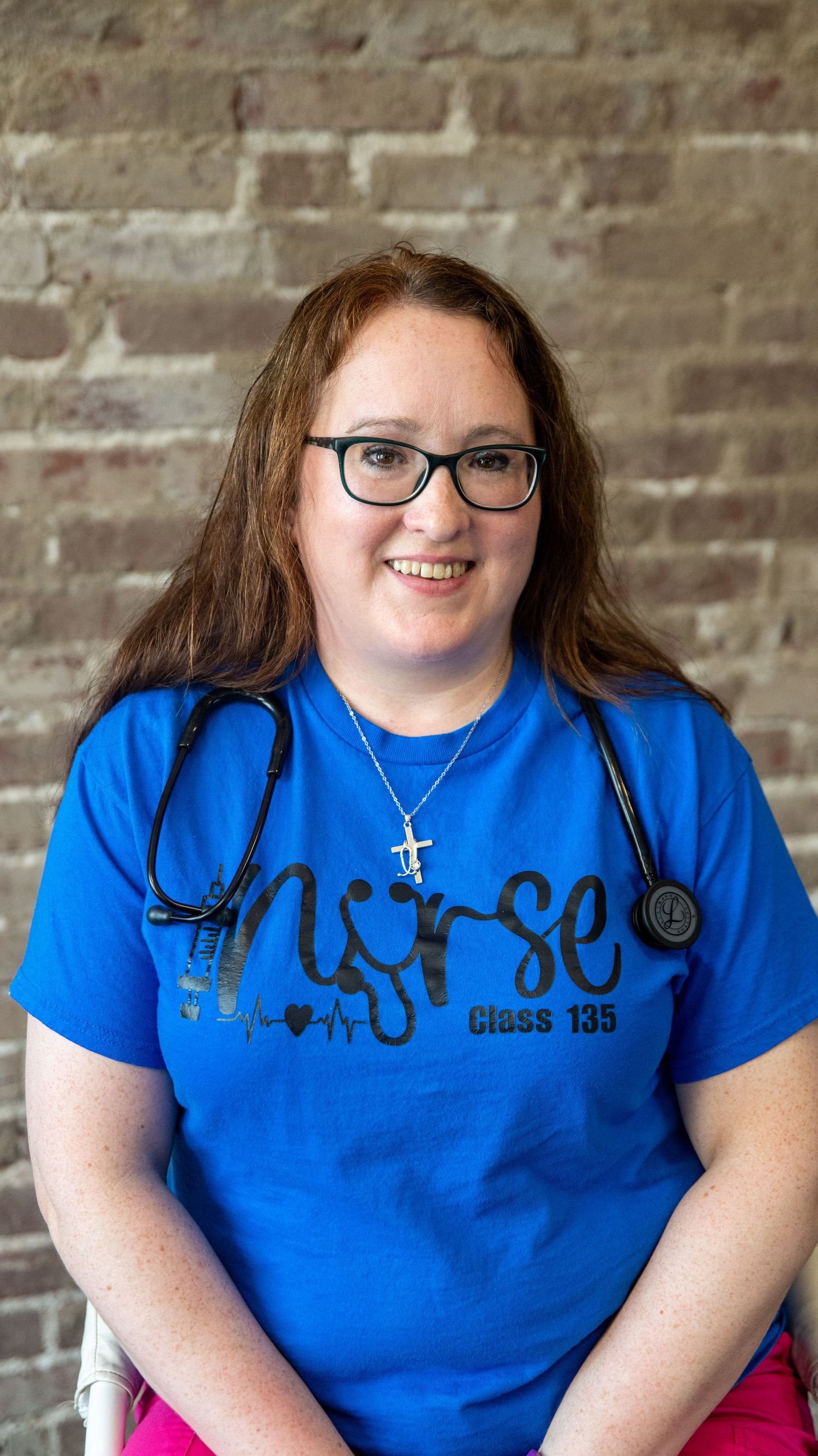 Person wearing a bright blue t-shirt with medical-themed design sits against a brick wall.