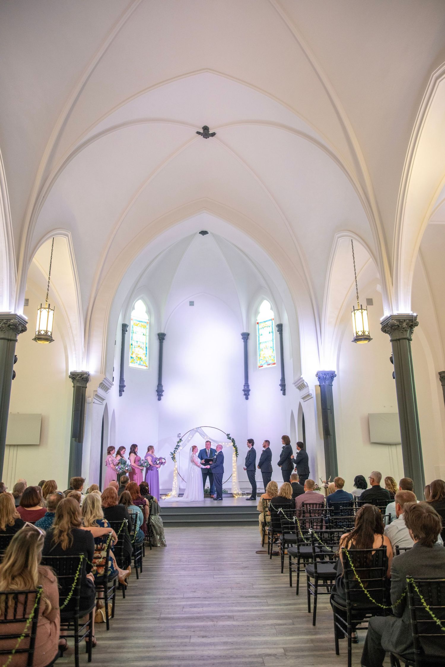 Wedding ceremony in a historic chapel with vaulted ceilings and gothic columns filled with seated guests.