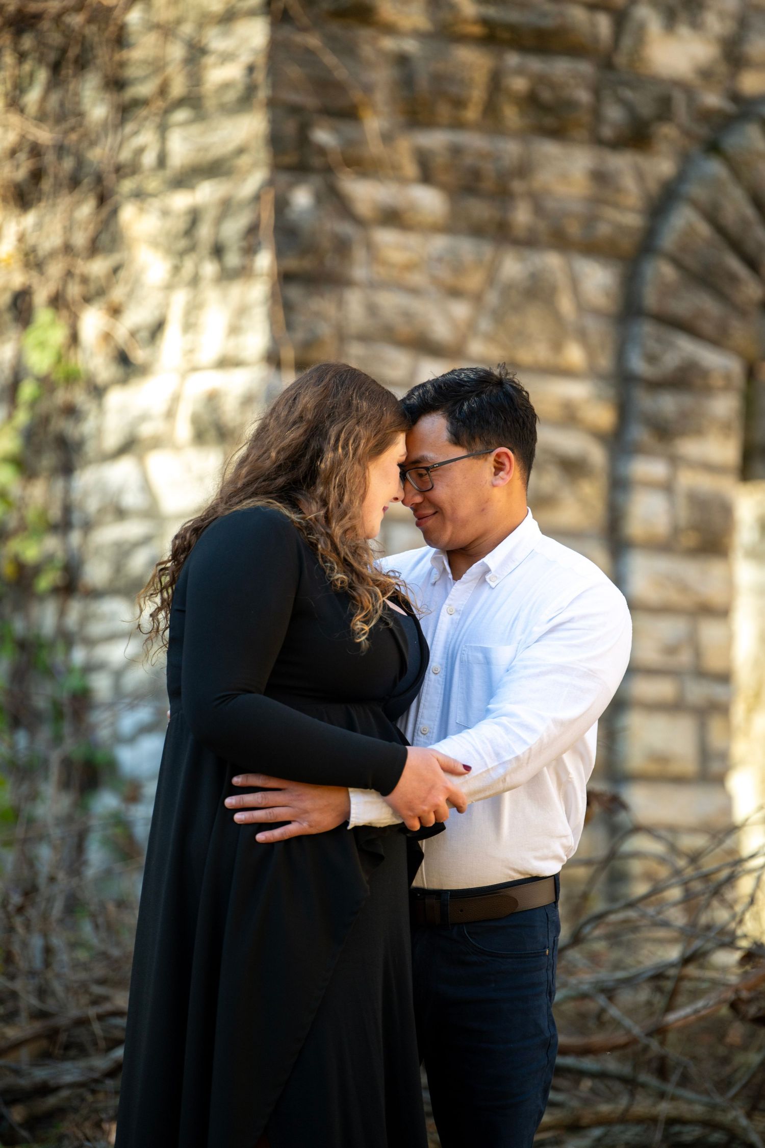 Couple embraces against rustic stone wall during autumn photo session.