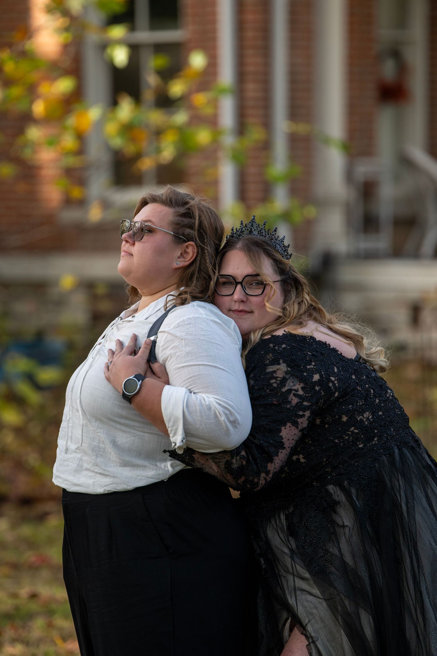 Two people in formal attire share an emotional embrace on autumn grounds.