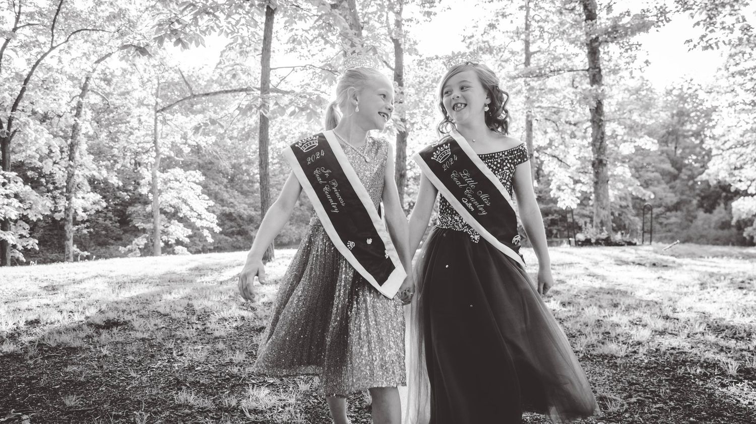 Black and white photo of pageant participants posing in an outdoor forest setting.