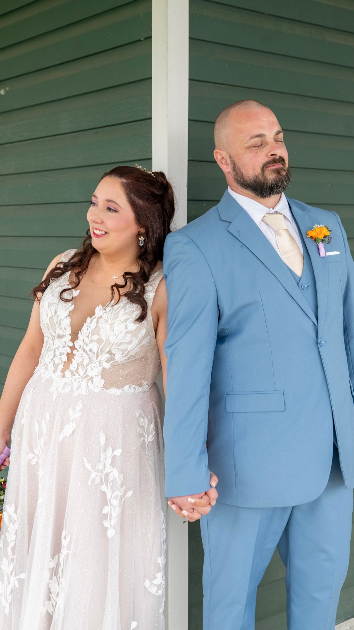 Wedding couple in blue suit and white lace dress sharing candid moments on porch.