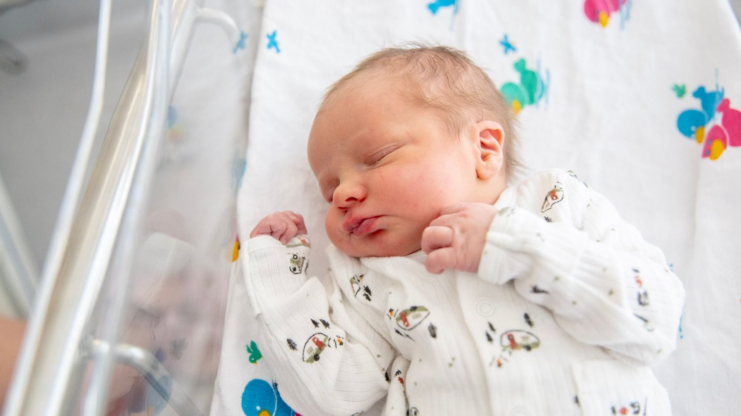 Newborn baby resting peacefully in hospital bassinet with colorful decorations.