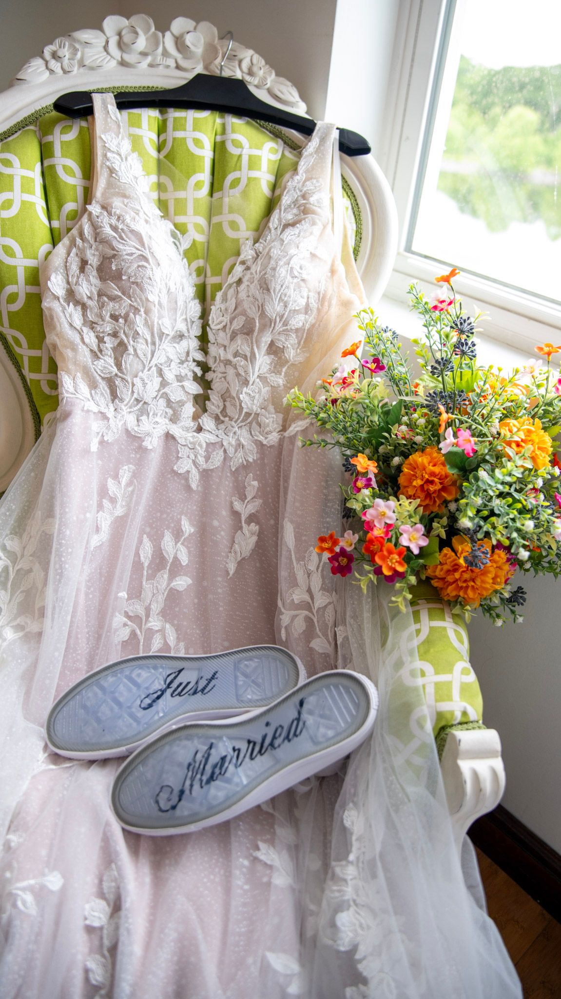 Wedding dress on hanger with floral bouquet and 'Just Married' shoe decorations.