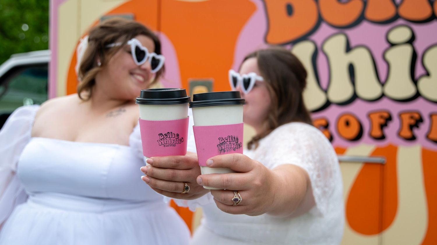 Close-up of coffee cups against blurred orange and pink signage.