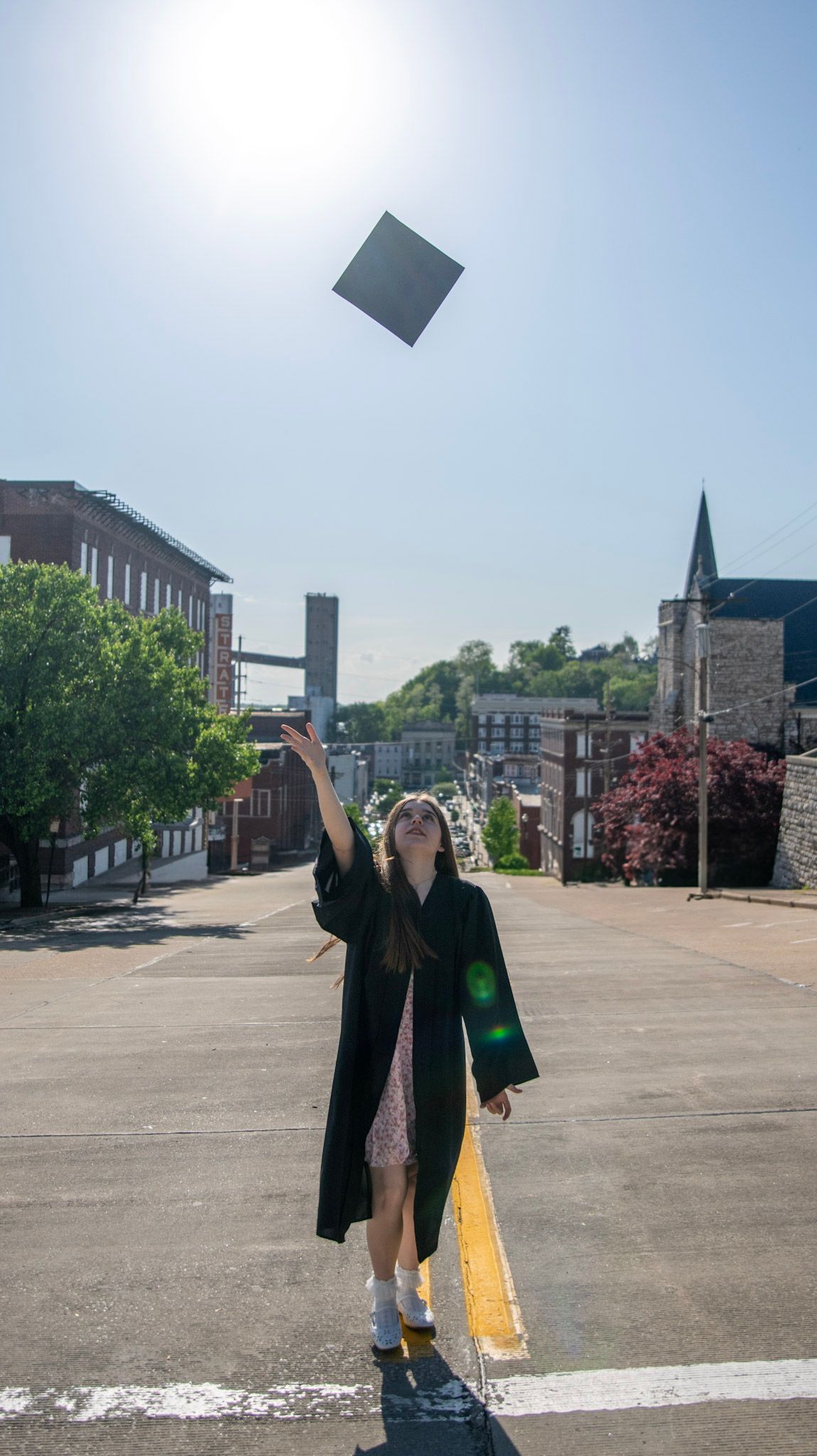 Sequence showing graduation cap toss against blue sky and urban buildings.