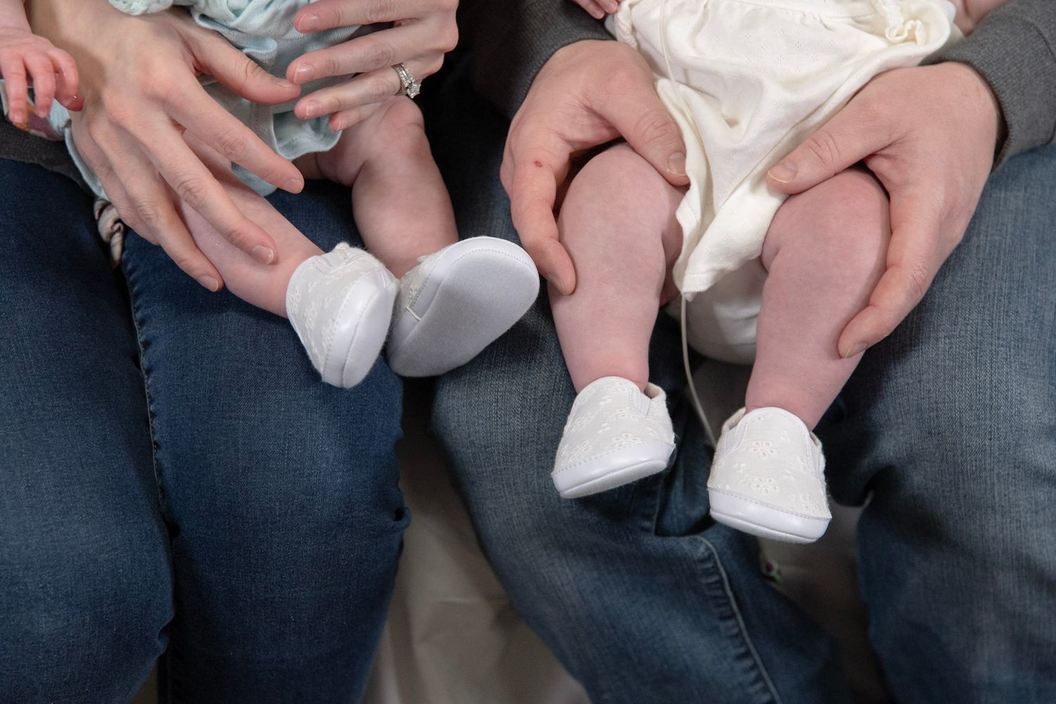 Close-up view of hands holding and supporting a baby wearing white clothing.