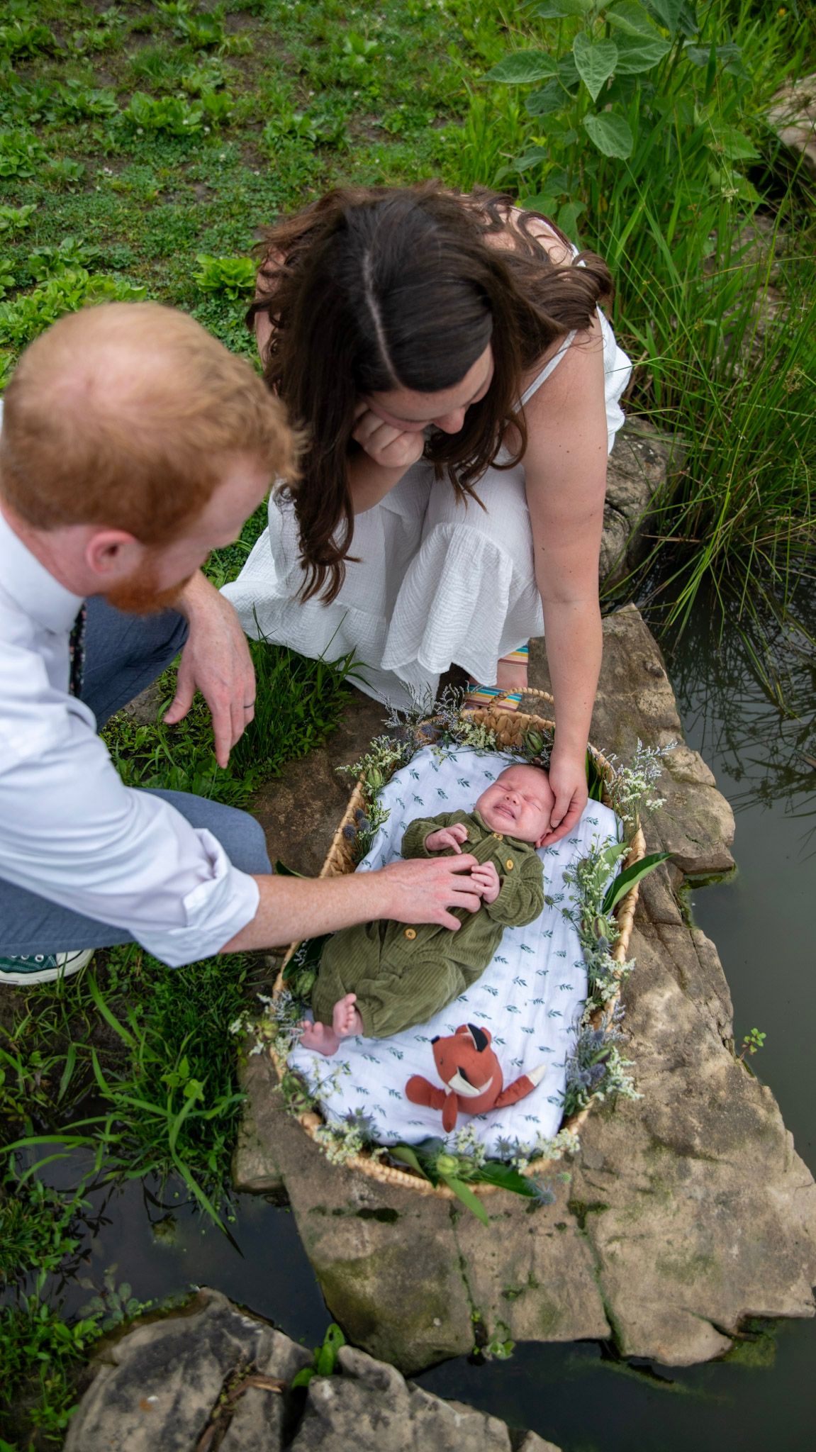 Parents carefully place their newborn in a decorated basket by the water's edge.