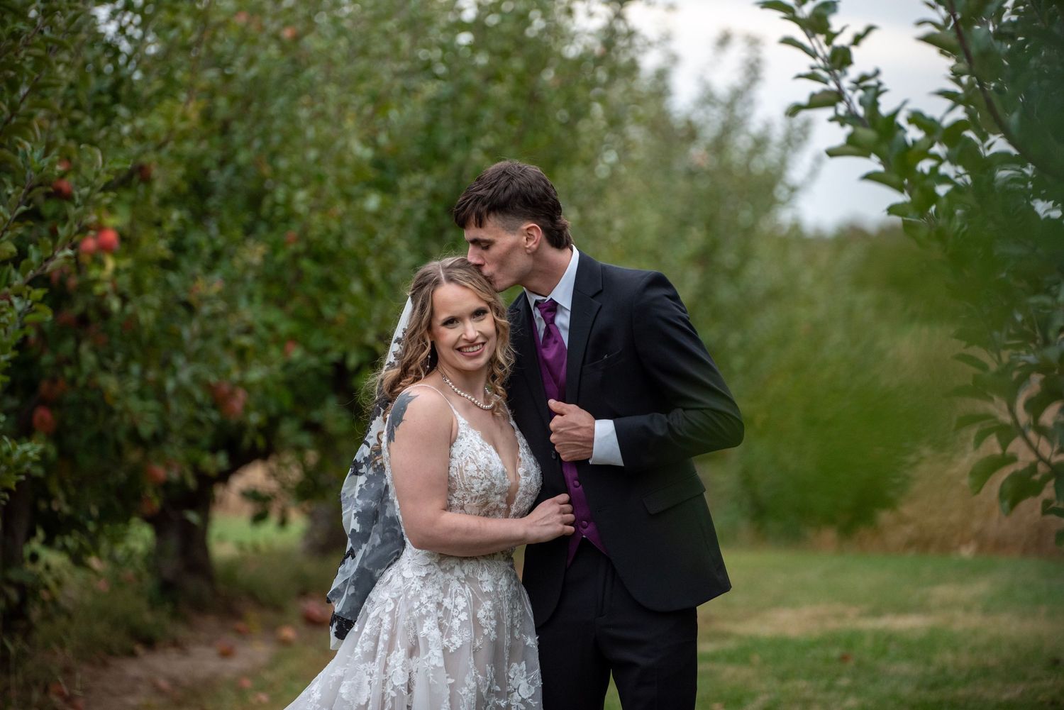 Wedding couple shares an intimate moment while standing between rows of apple trees in an orchard.