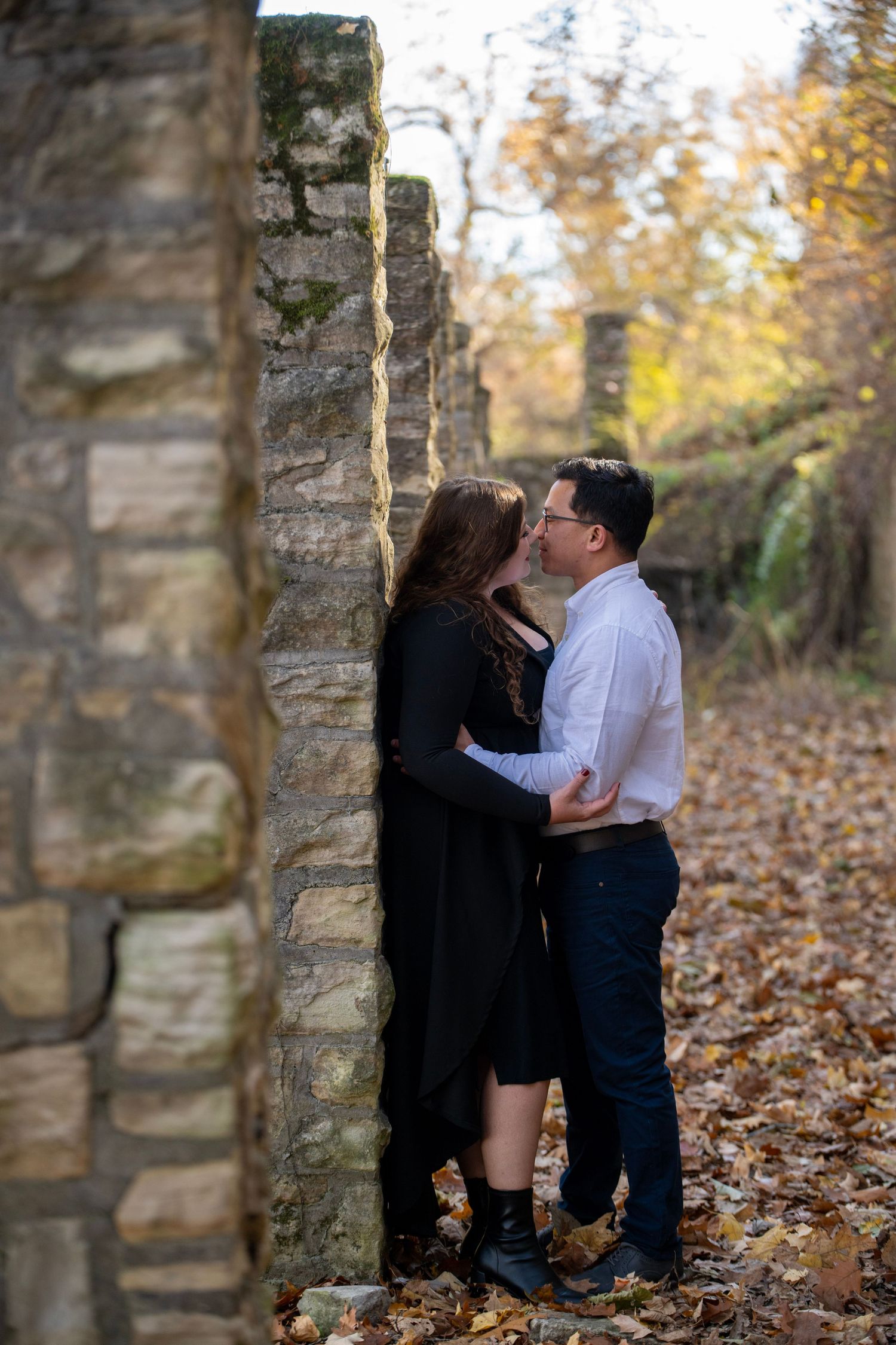 A tender moment between a couple among historic stone columns surrounded by autumn leaves.