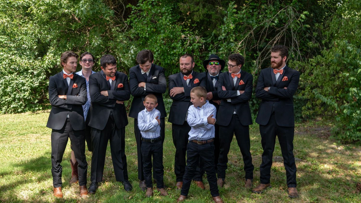 Wedding party in formal attire posing together outdoors against a green natural background.