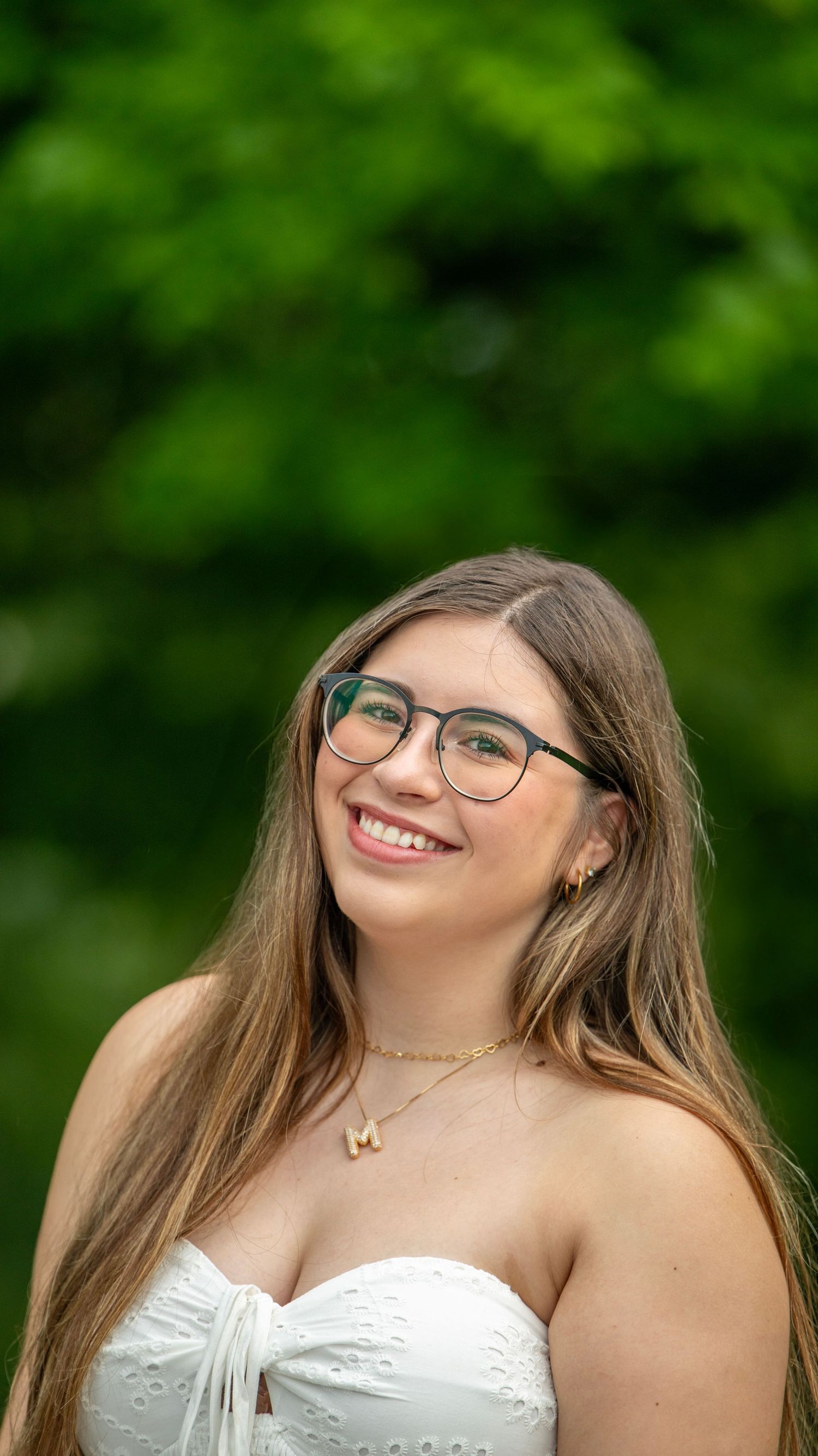 A person in glasses and white dress smiles warmly against a green background.