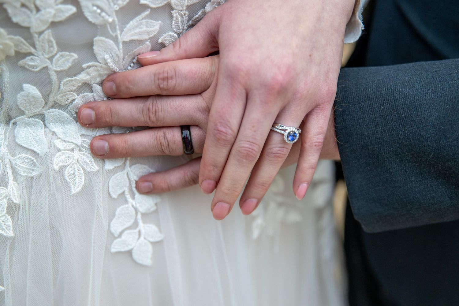 Close-up of hands displaying wedding rings against a white lace background.