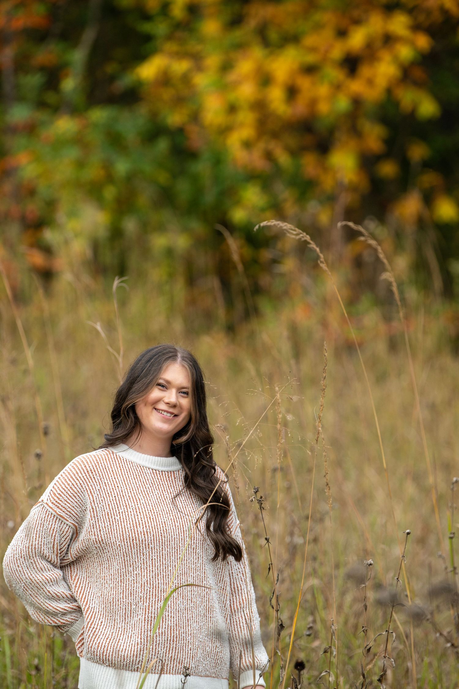 A candid outdoor portrait captures someone laughing in a beige sweater against fall colors.