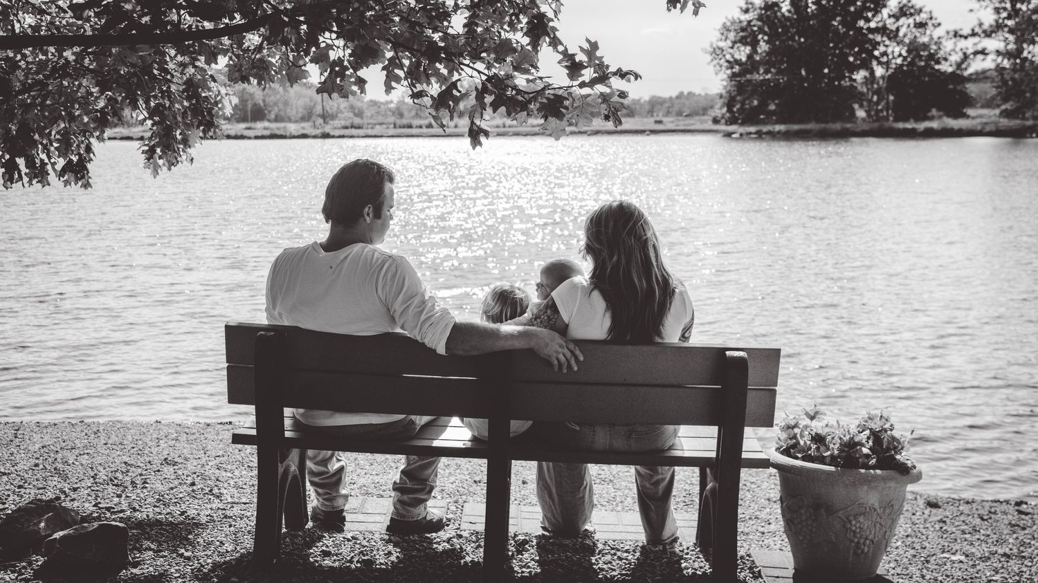 Black and white panoramic of people sitting on bench overlooking serene lake.