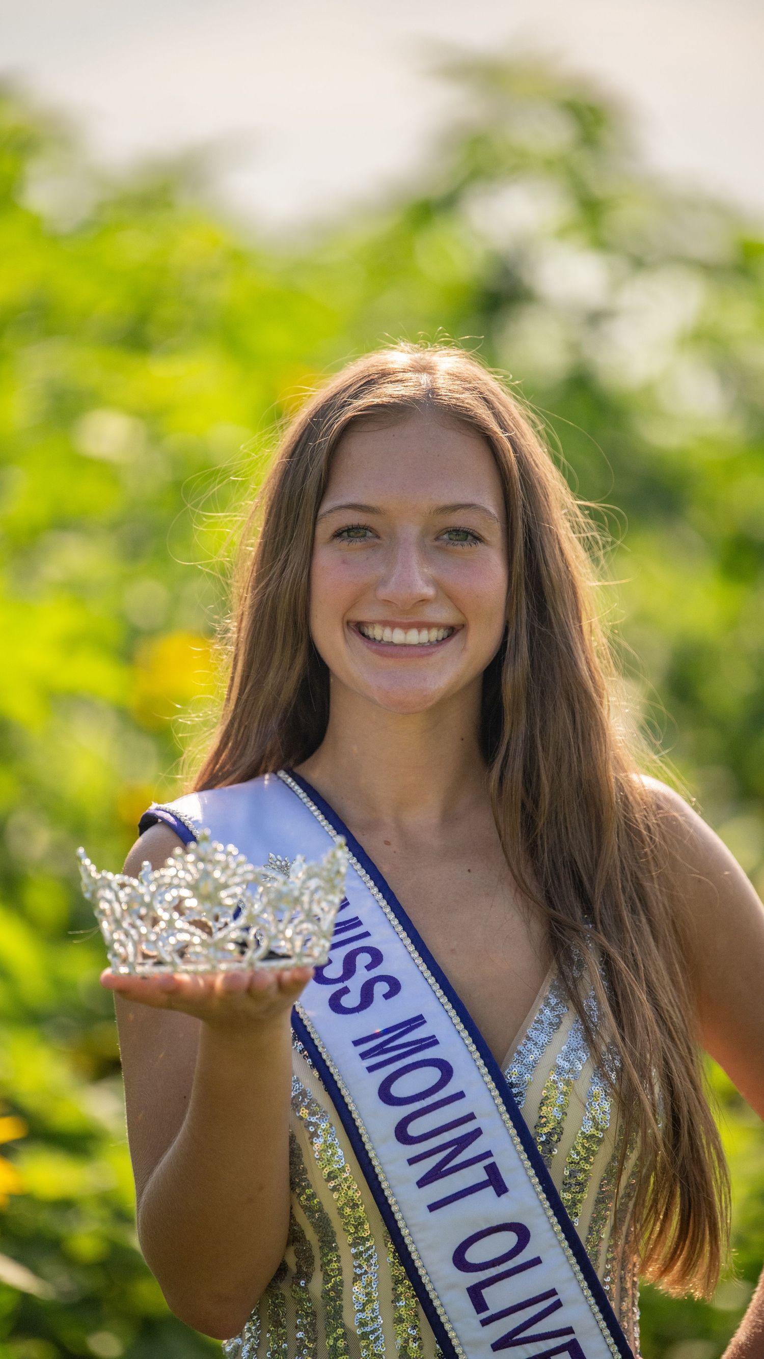 A pageant winner displays her crown while wearing a sparkly dress and sash.