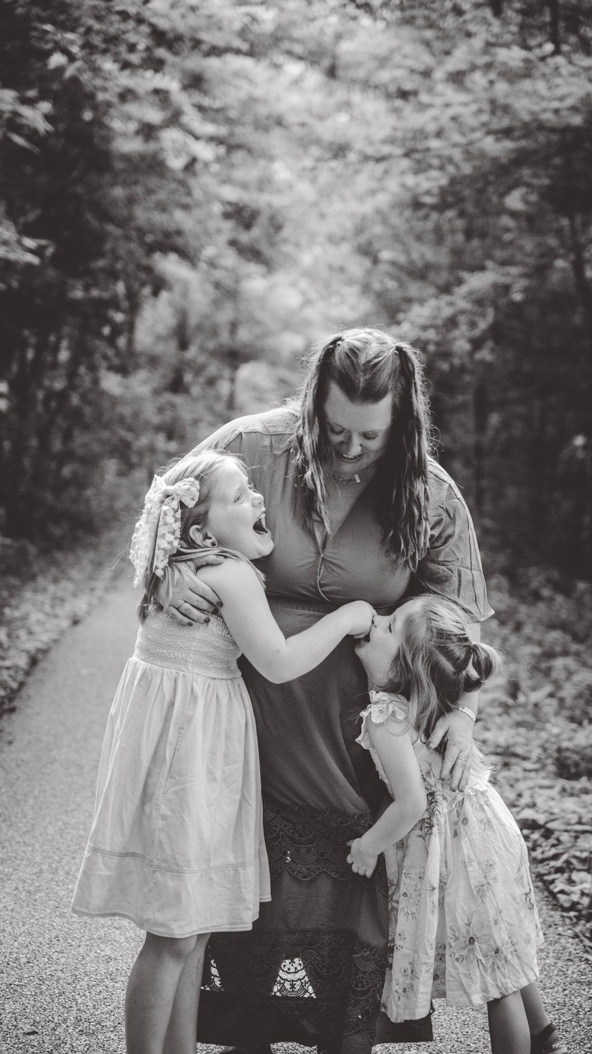 A heartwarming family embrace captured in black and white on a forest path.