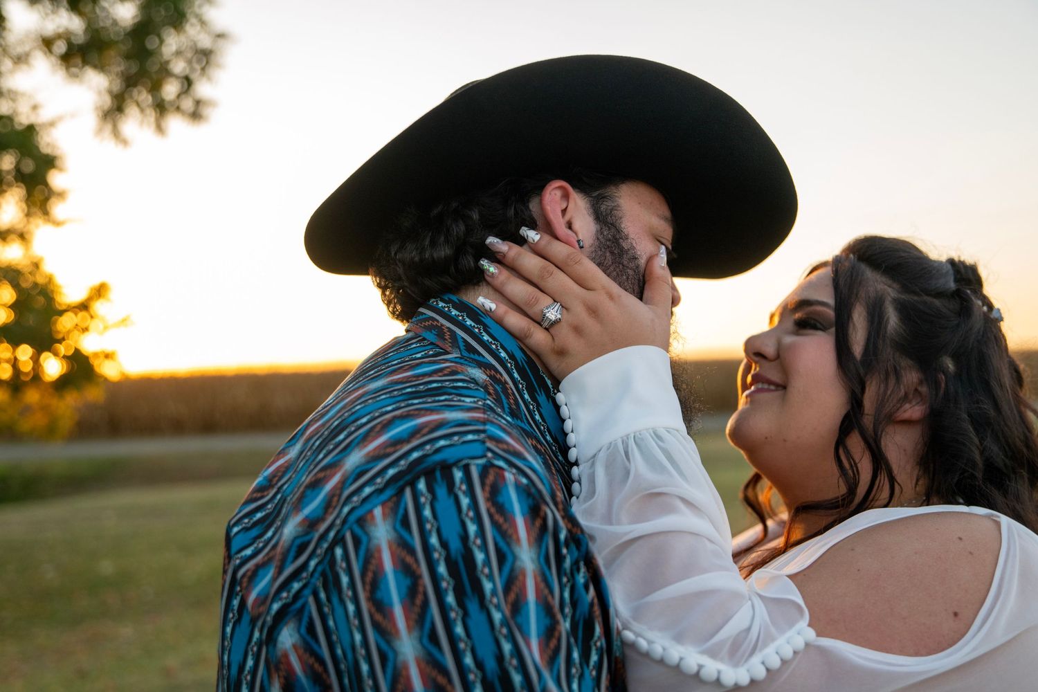 A couple sharing an intimate moment at sunset, with one wearing a western hat and blue patterned shirt.