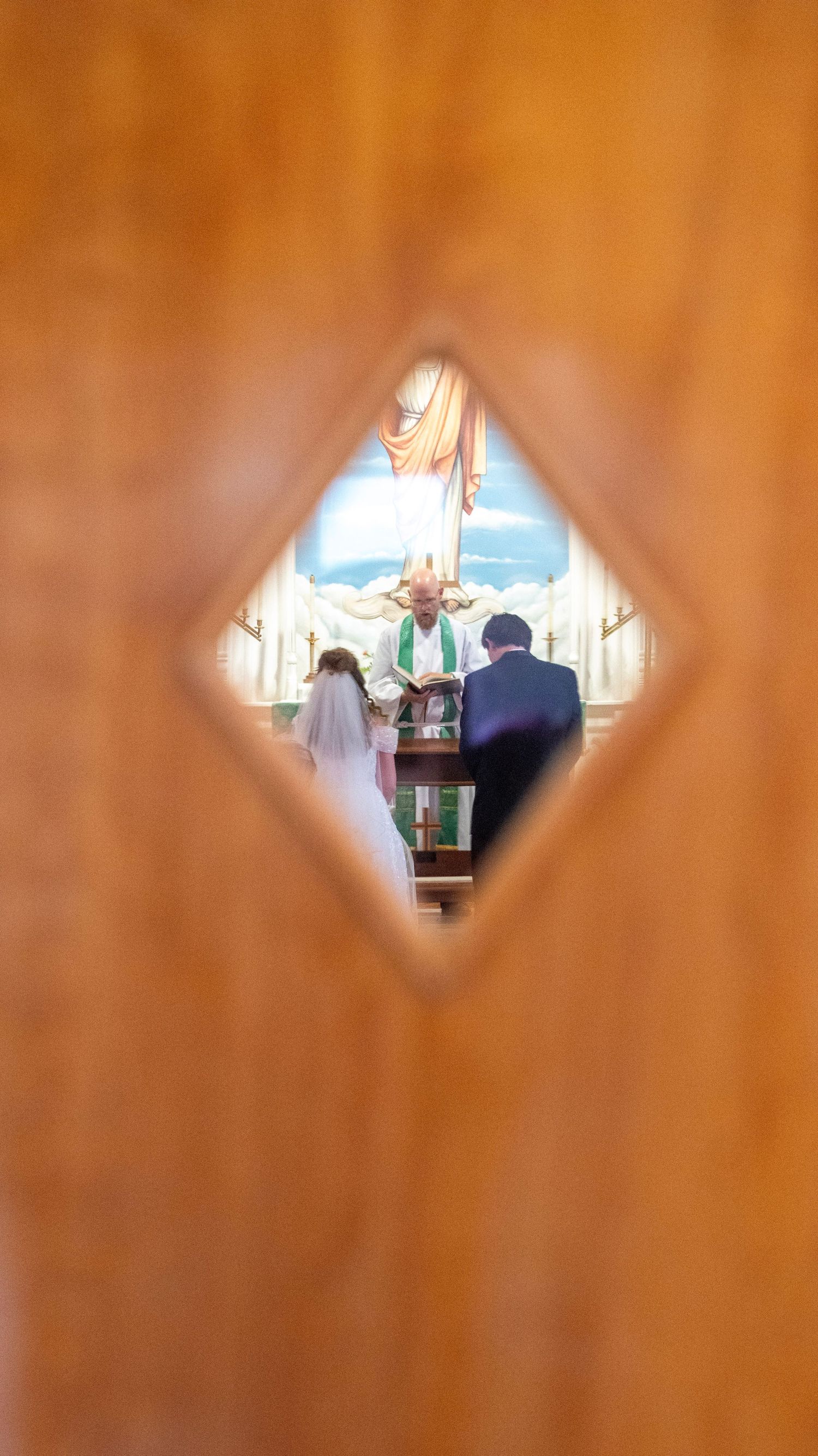 Diamond-shaped peepholes in wooden church doors offering glimpses of a wedding ceremony.