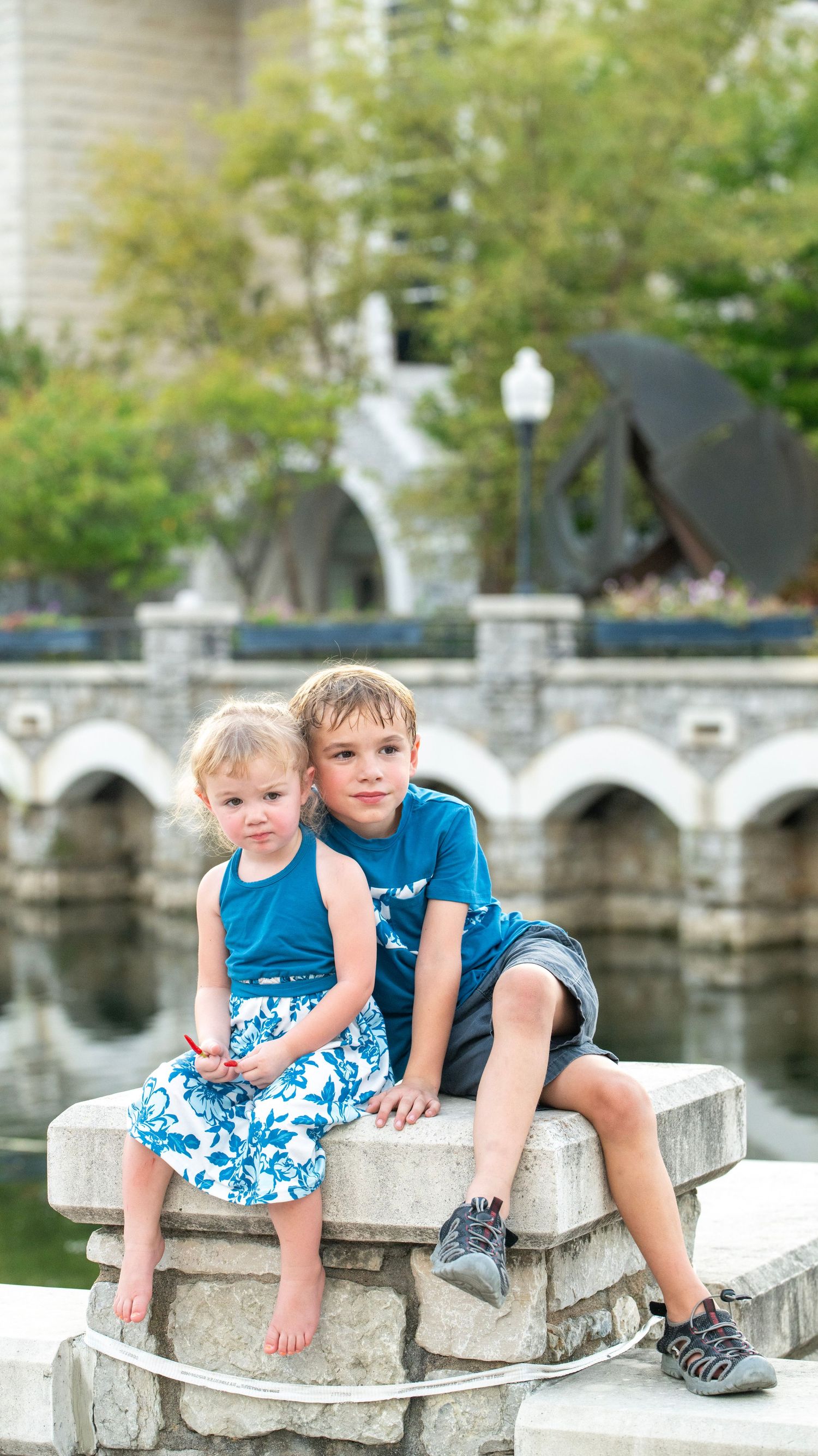 Children sitting together on decorative stone wall near arched architecture.
