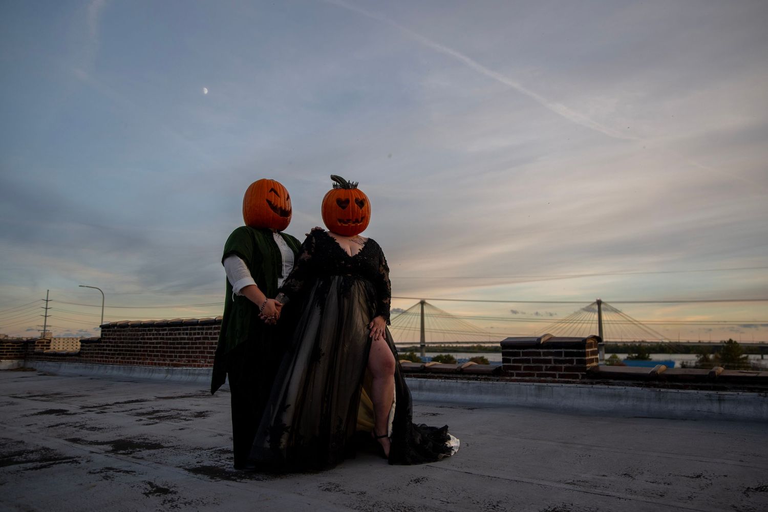 Two pumpkin-headed figures in period dress sitting together on rooftop at dusk.