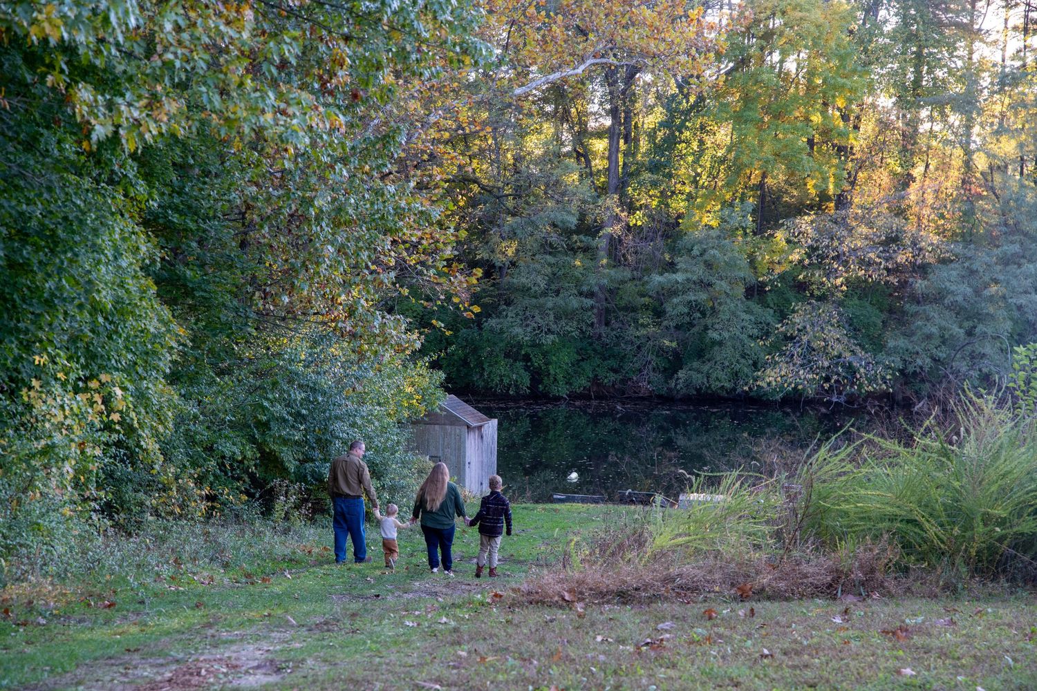 Three figures walk along a wooded trail during peak fall foliage season.