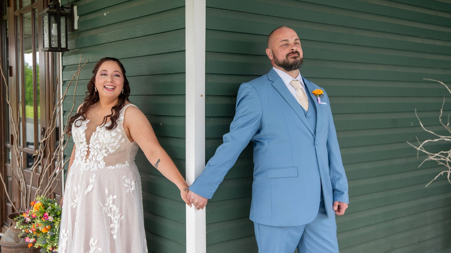 Wedding couple posing against green exterior wall in formal attire.