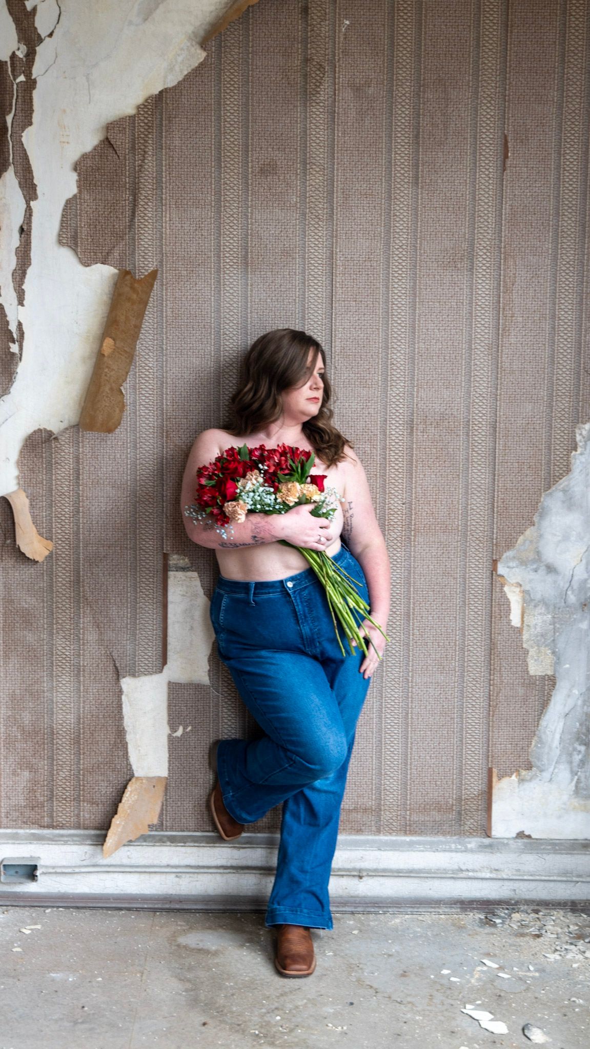 Intimate portrait against vintage wallpaper with red rose bouquet.