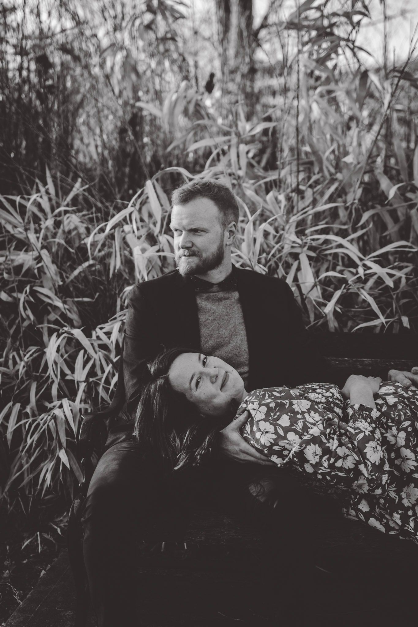 Black and white portrait of couple on bench with dramatic lighting and natural backdrop.