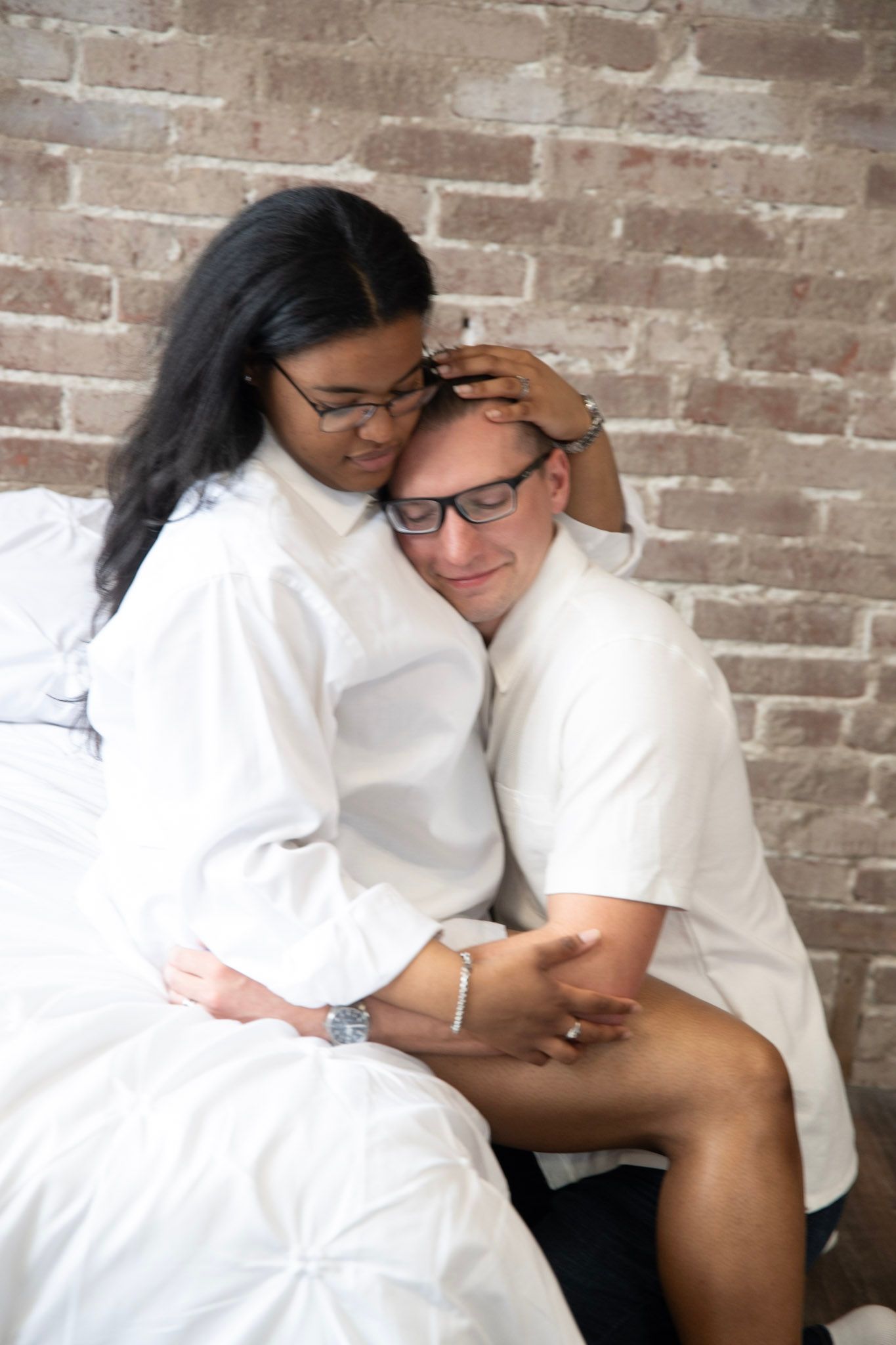 Tender moments captured during couple's photoshoot against exposed brick wall.