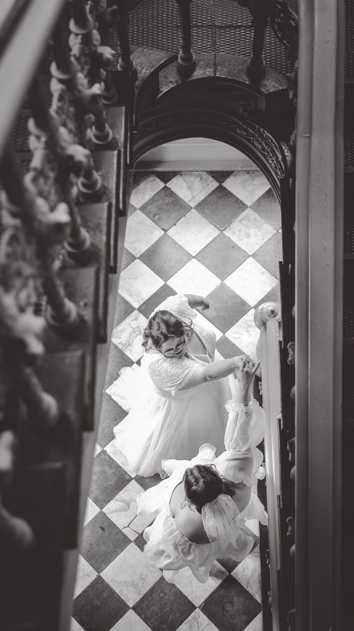 Overhead shot of two people in white gowns embracing on a geometric tiled floor.