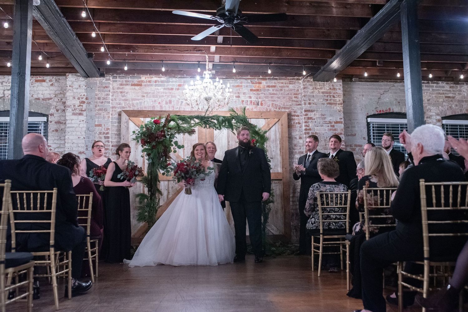 An indoor wedding ceremony with guests seated in a rustic brick venue.