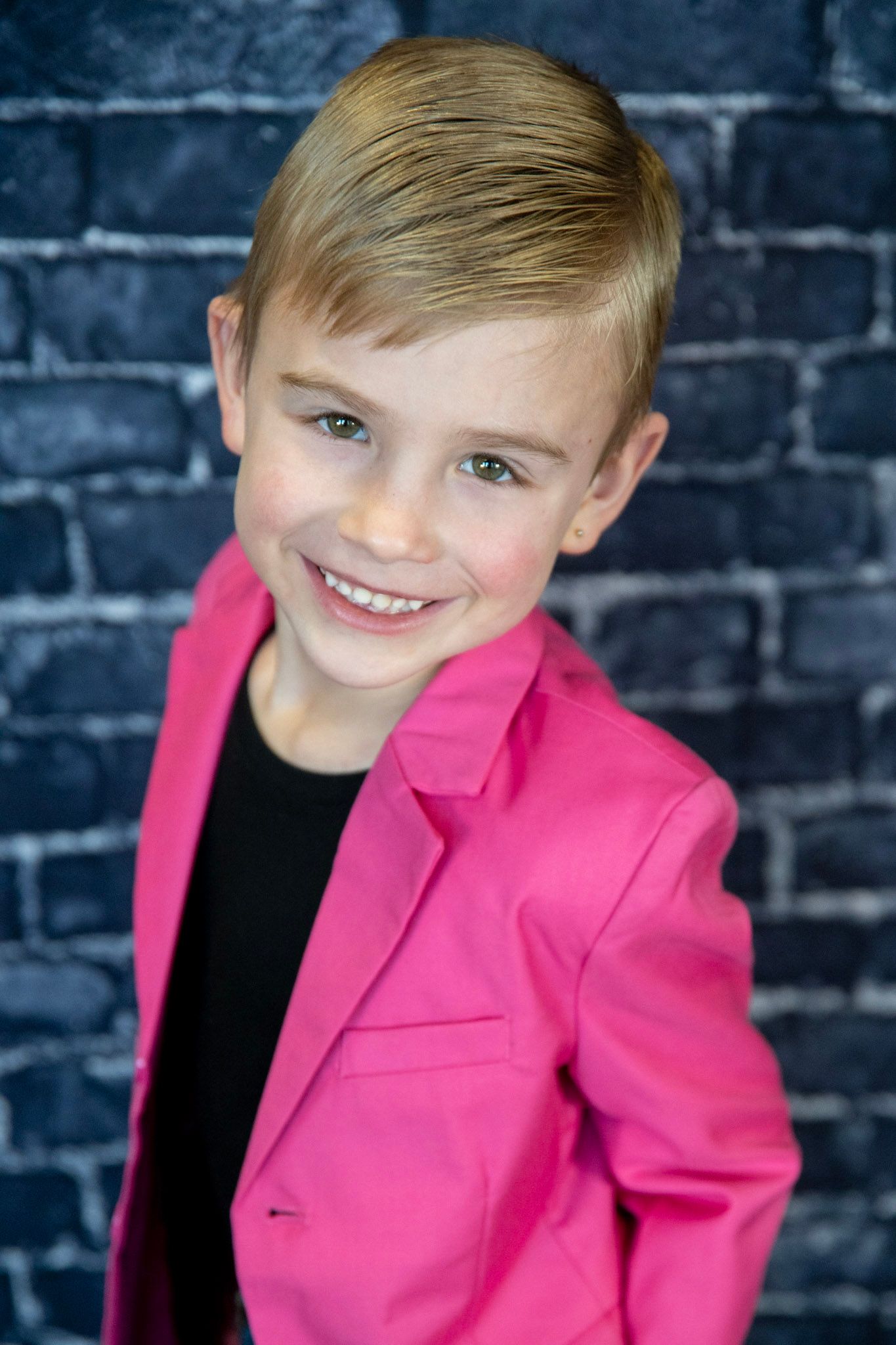 Cheerful expressions captured against a dark brick wall while wearing a bright pink blazer.