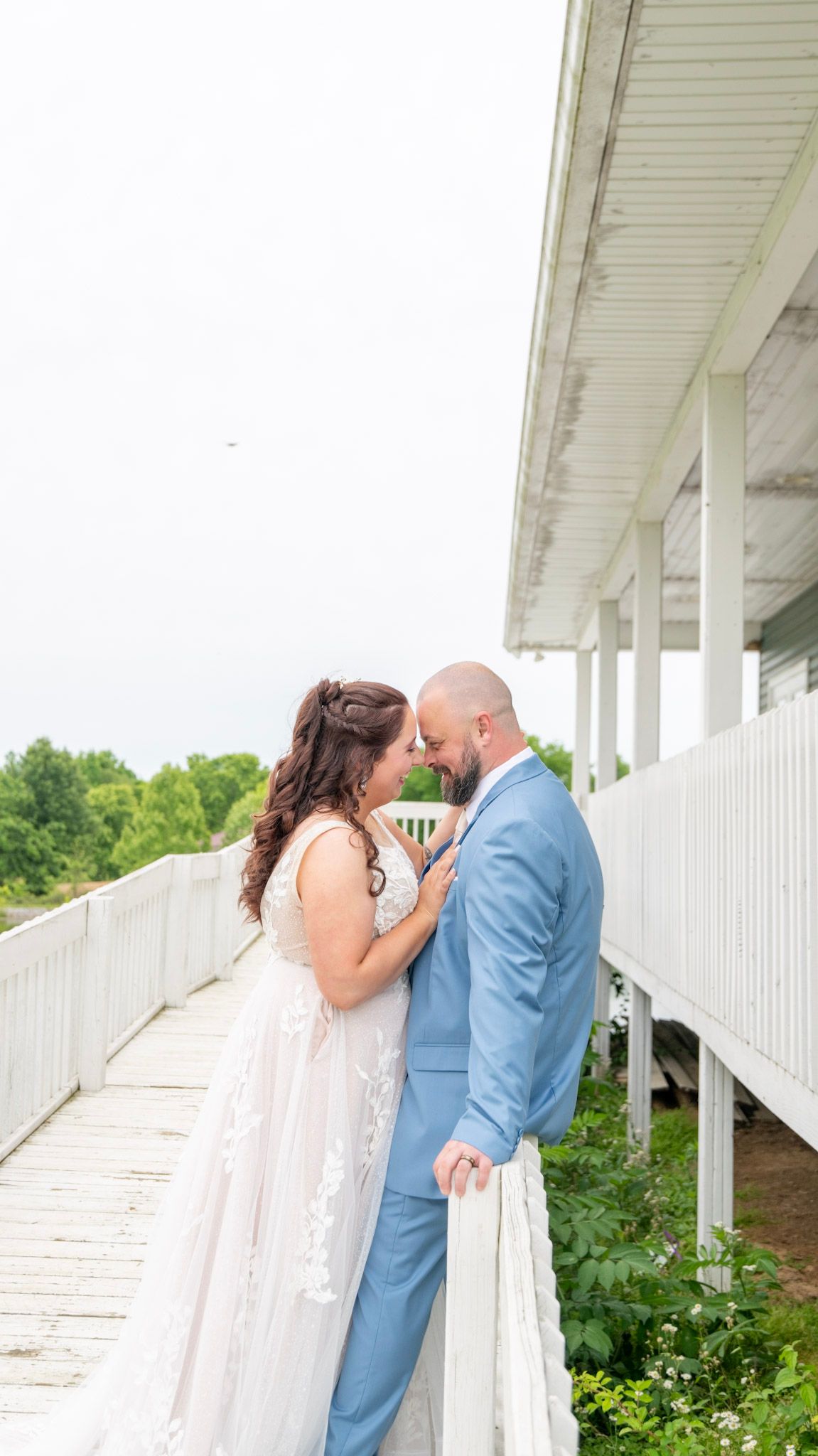 Wedding couple sharing intimate moments against a white porch backdrop.
