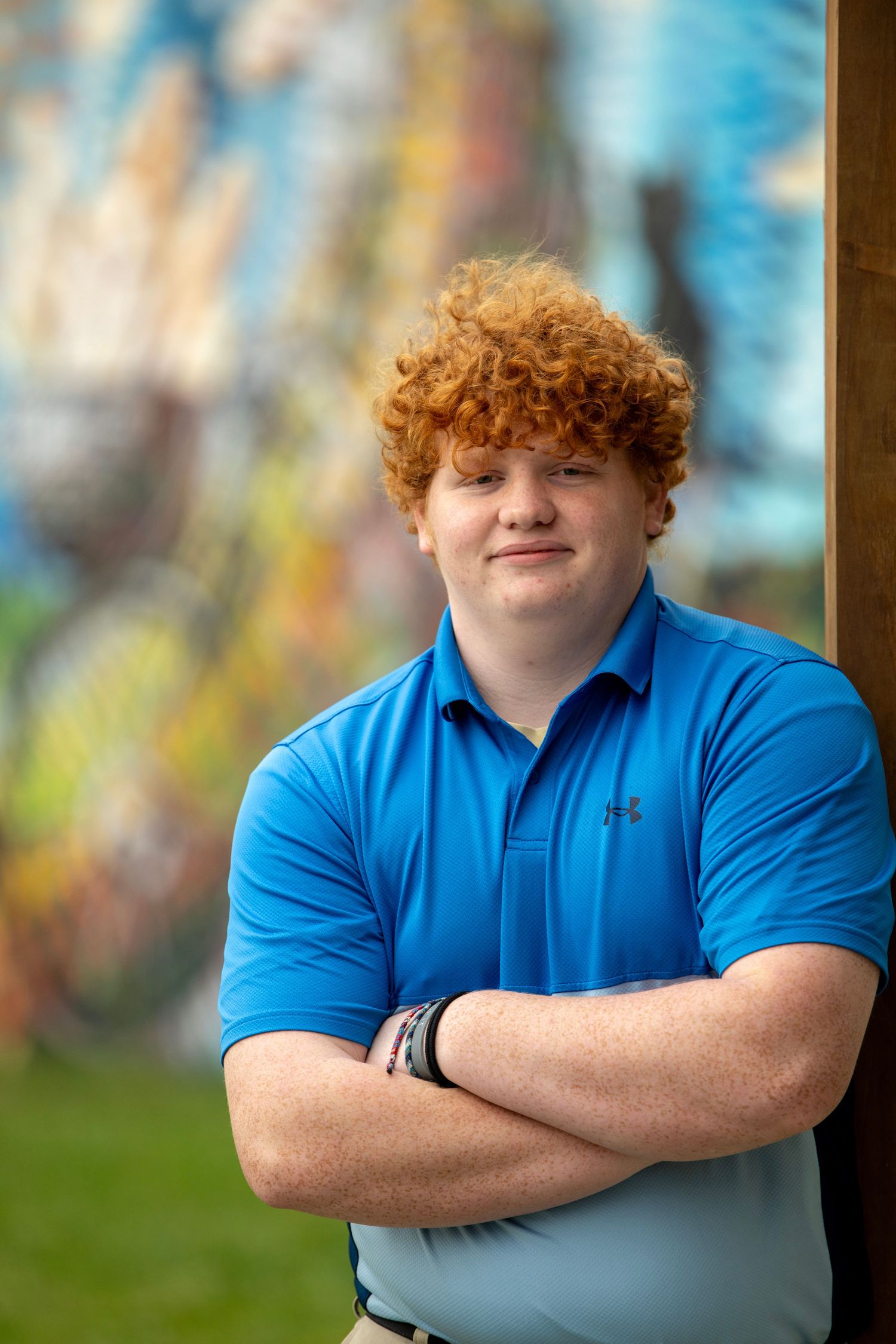 Professional headshots with arms crossed in blue polo shirt against colorful background.