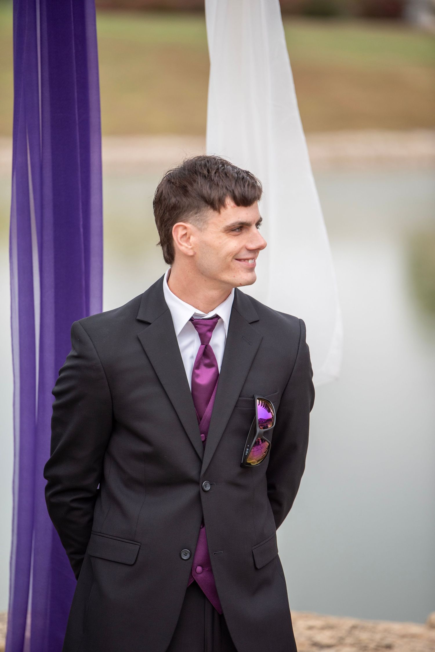 Groomsman in black suit with purple tie posing by purple and white wedding decor.