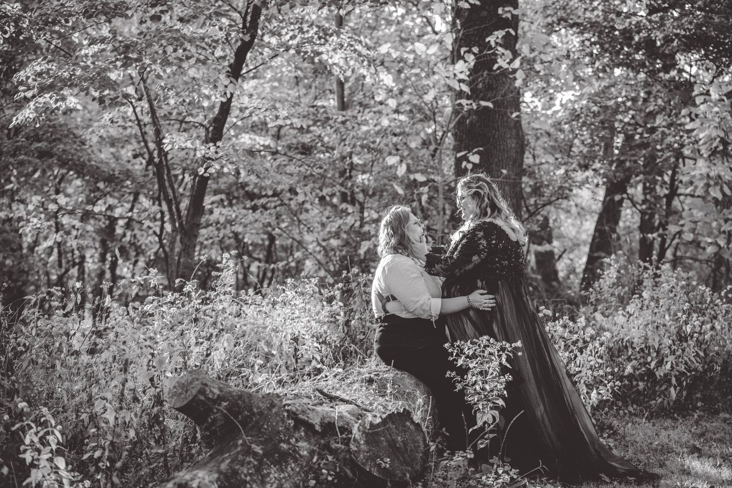 Black and white photo of a couple embracing in a wooded area.