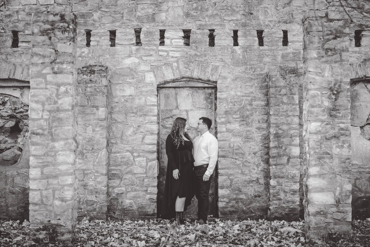 Stone wall archways create rustic backdrop for romantic autumn engagement photos.