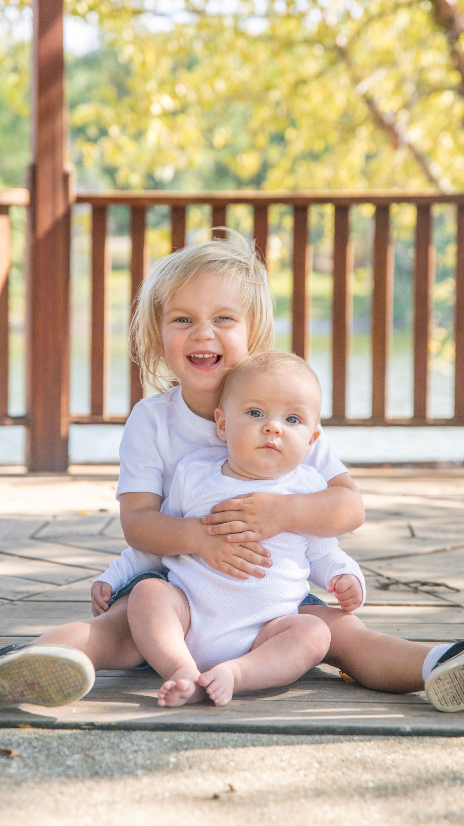 Heartwarming sibling portrait with matching white shirts on a sunny porch.