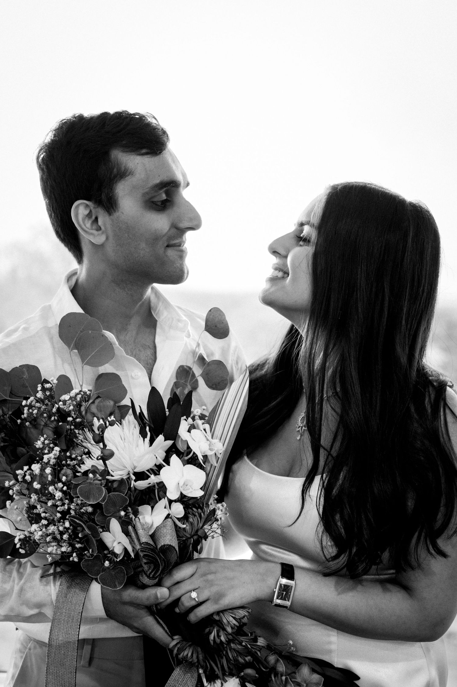 A romantic black and white portrait of a couple sharing a joyful moment with a bouquet of flowers.