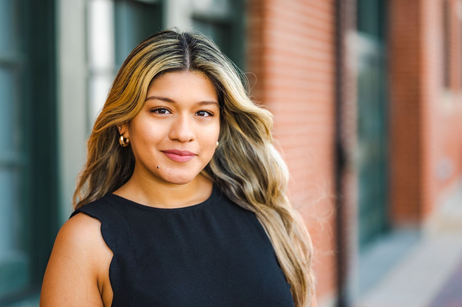 Professional headshot portrait against an urban brick building background.