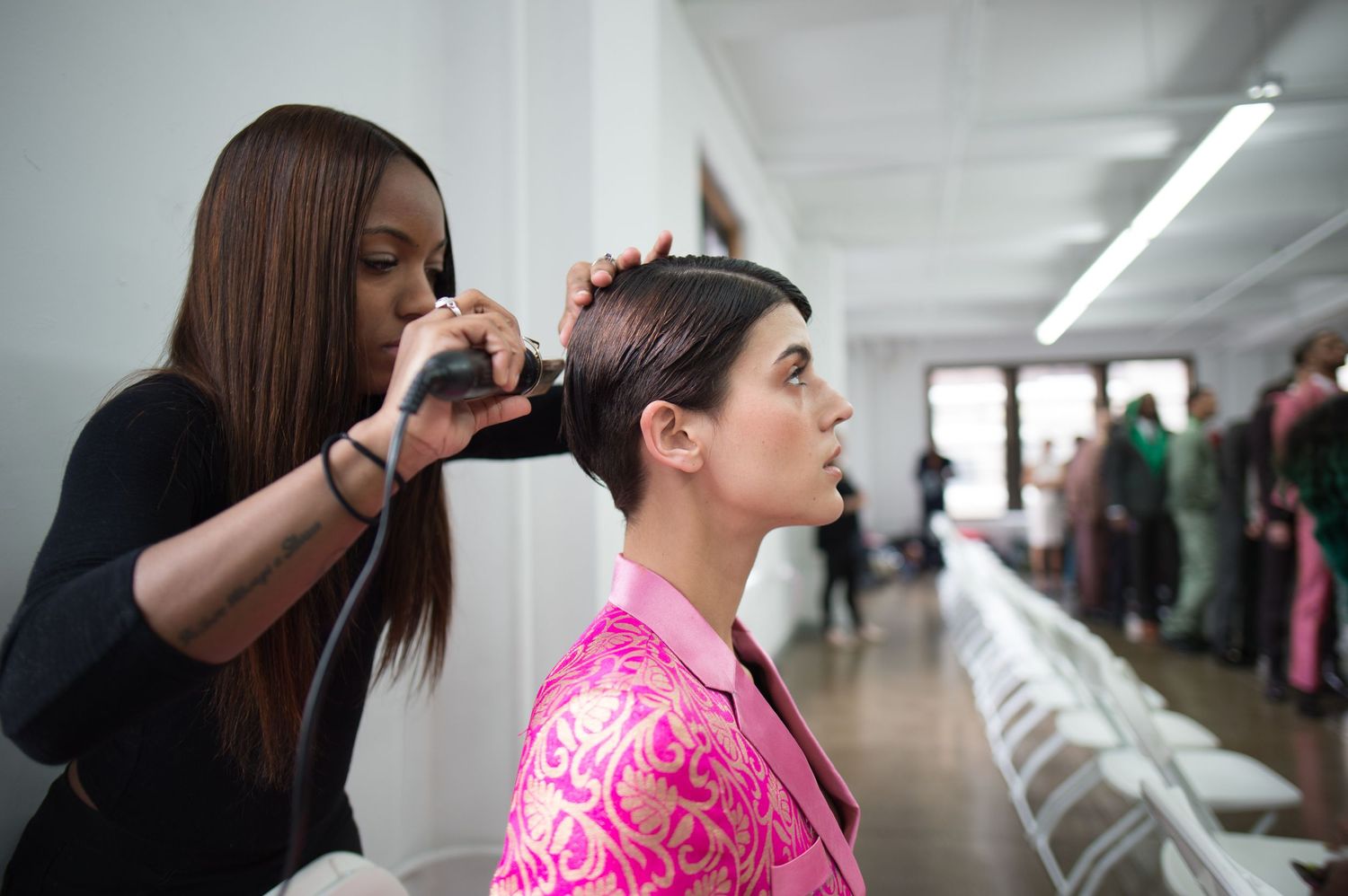 A person in a bright pink patterned top receives a professional hair styling service in a modern salon.