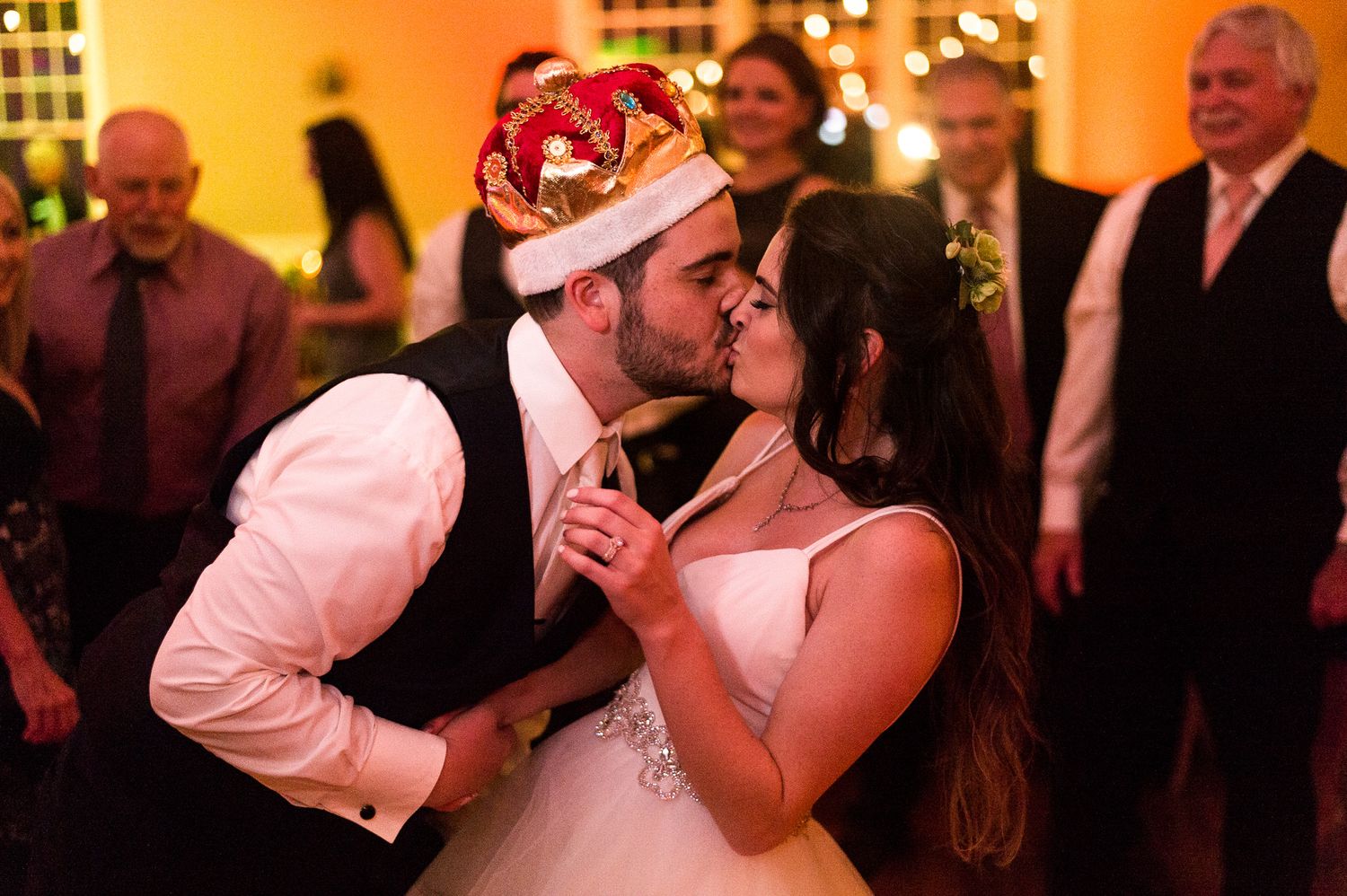 A couple shares a romantic moment during their wedding reception as the groom wears a festive Santa hat.