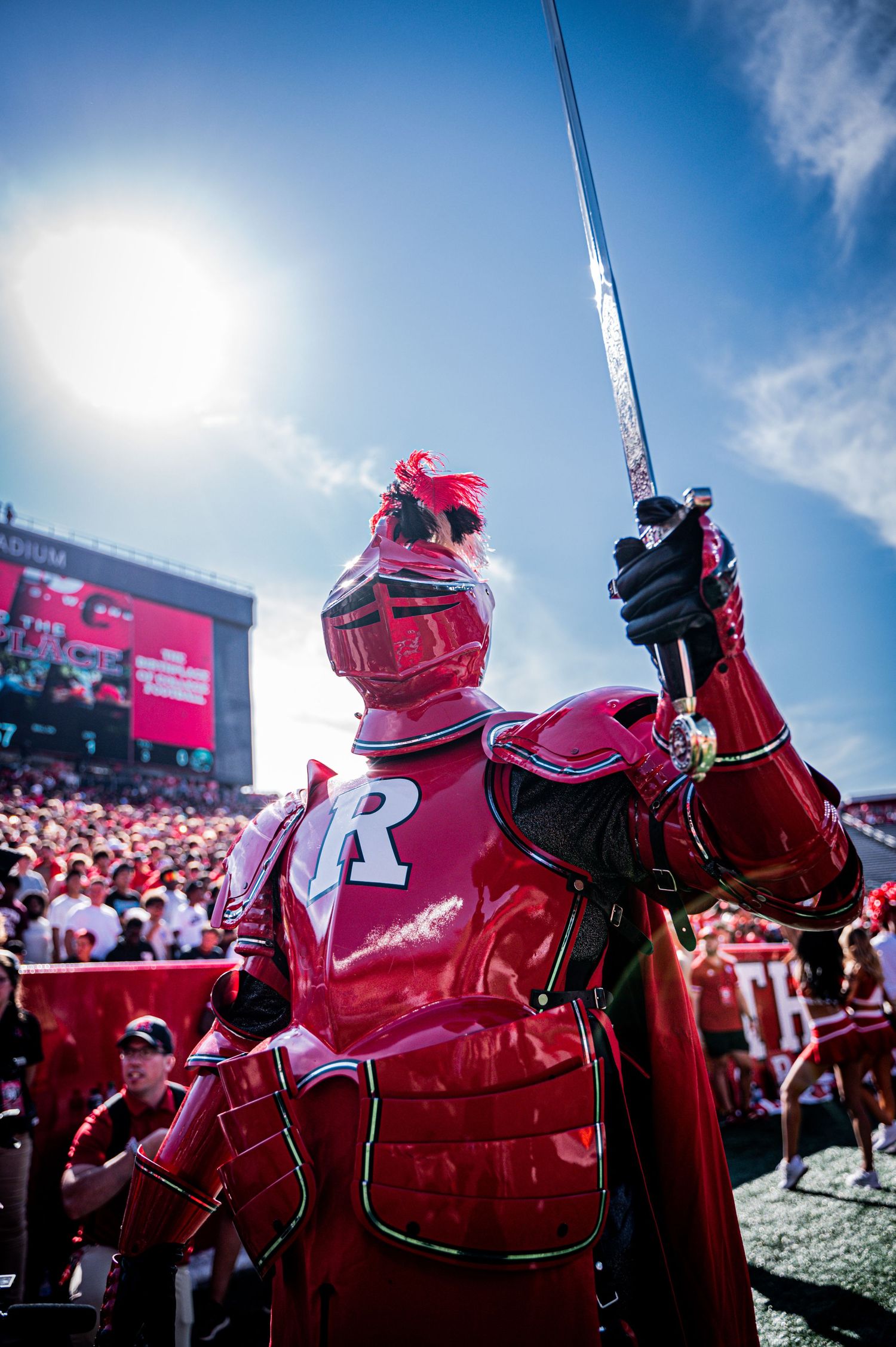 Red mascot figures silhouetted against bright blue sky at a Nebraska Cornhuskers football game.
