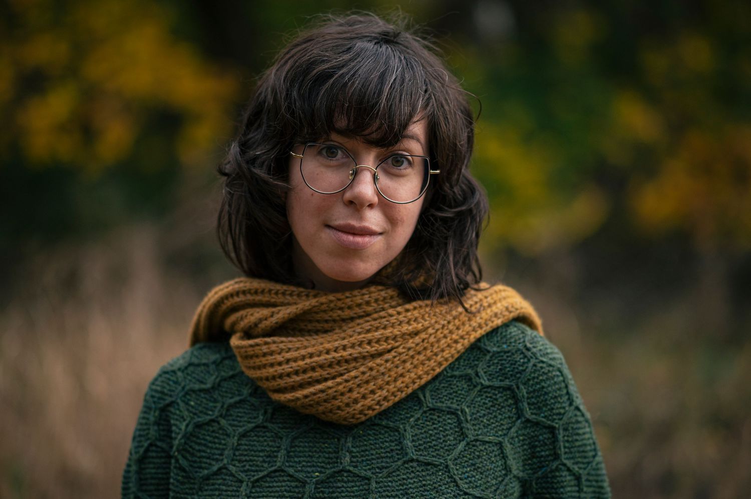 Winter fashion portrait featuring knit scarf and glasses in natural setting.