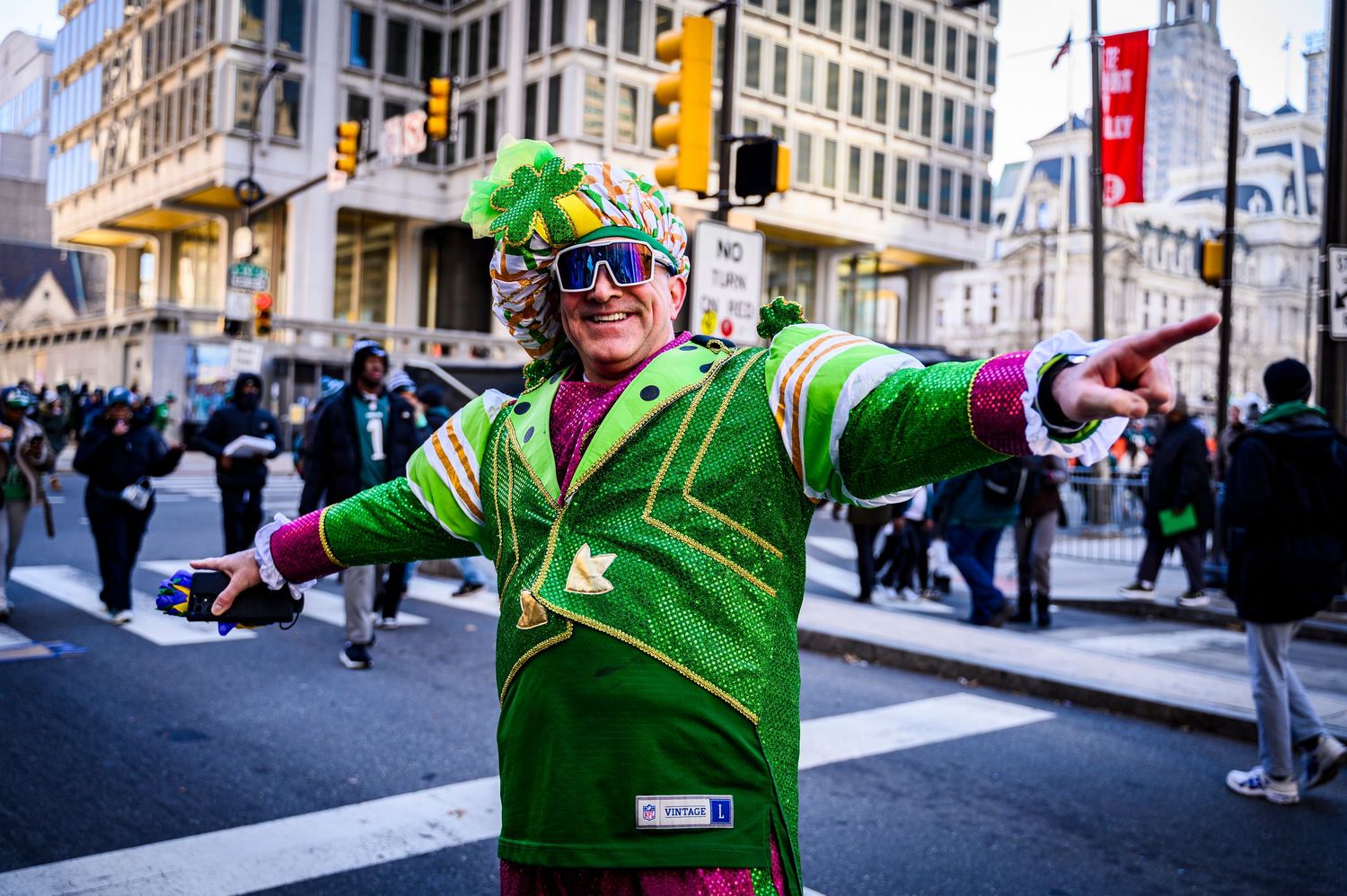 Performer in bright green costume dances energetically through city streets during a festive parade celebration.